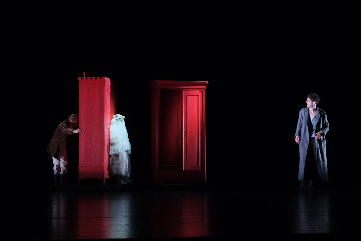 Swidrigajlow und Raskolnikow in einer dunklen Szene am Schauspiel Stutgart: zwei rote Kleiderschränke im dunklen Streiflicht schaffen einen bedrohlichen Ort.