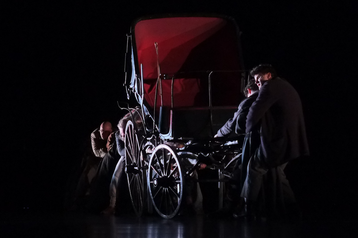 Theaterszene am Schauspiel Stuttgart: Das Ensemble versucht verzweifelt eine alte Kutsche zu ziehen und scheitert.