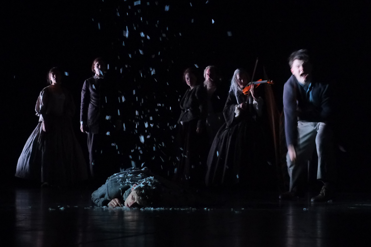 Surreale Szene am Schauspiel Stuttgart: Raskolnikovs Albtraum vom Pferd, er liegt im Schnee, Sonya, Porfiry, Dunya und Marmeladov starren ihn an und Rasumichin peitscht wie besessen auf den Boden.