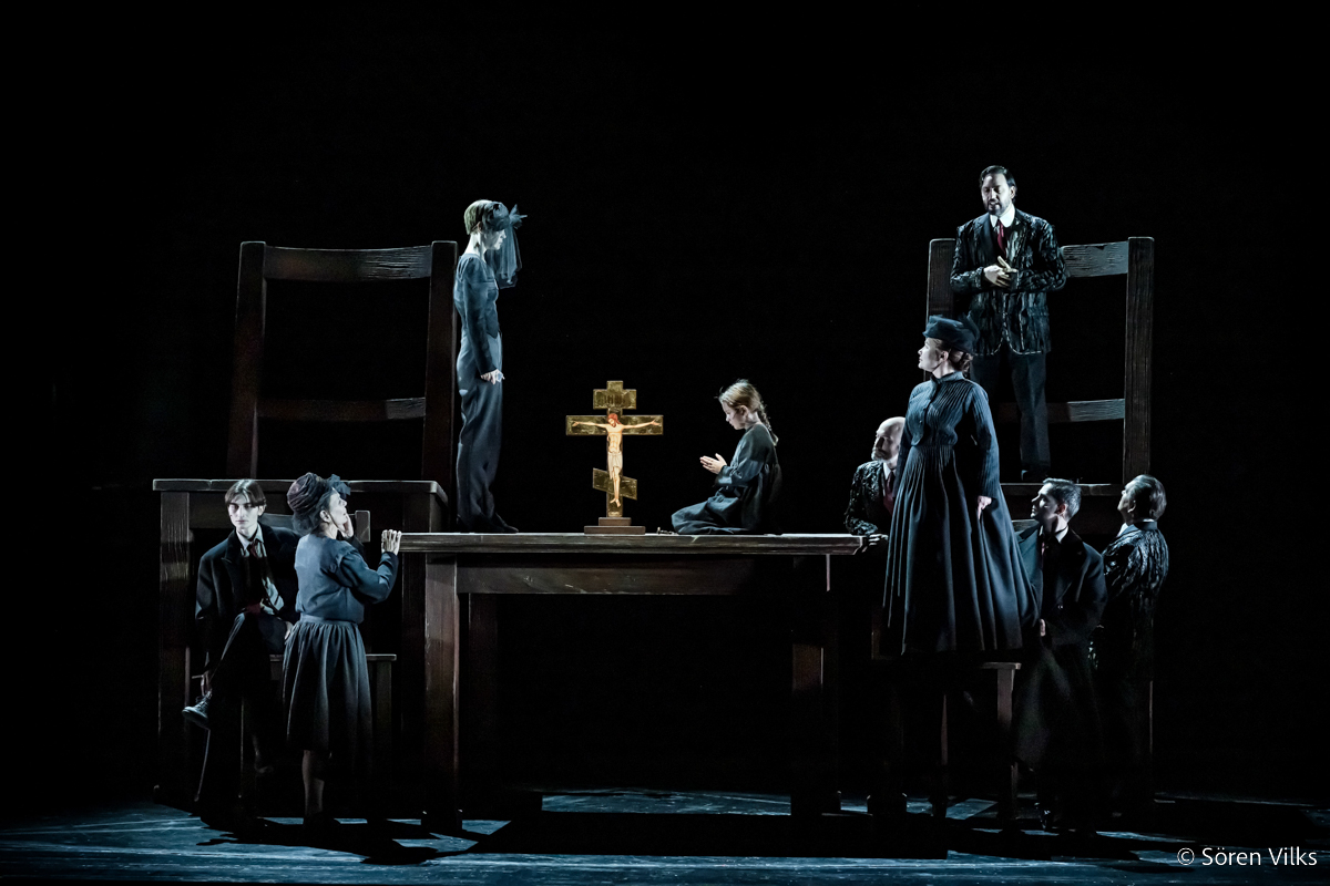 Theater scene evoking Renaissance painting: Sofya Semyonovna on a monumental table, under the glow of dark yet brilliant light, witnessing Polenka's prayer to a golden cross while 'Crime and Punishment' characters look on at Dramaten