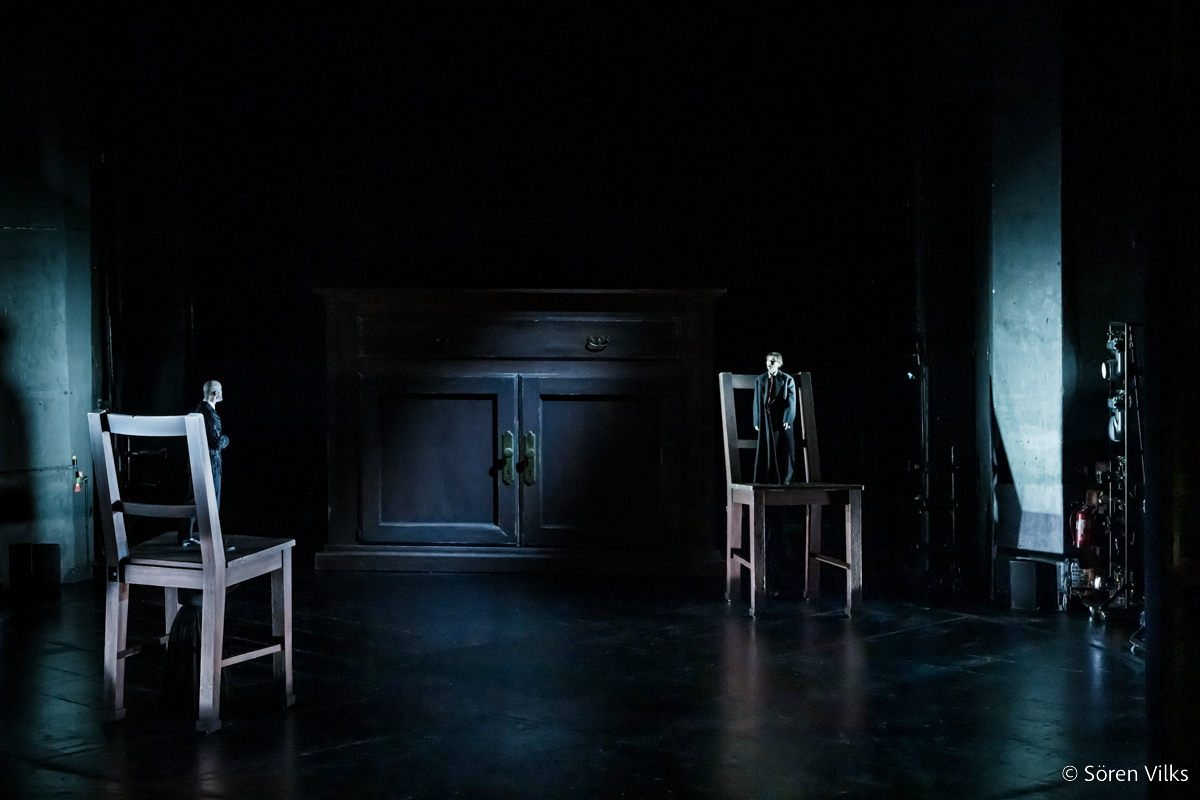 Rodion Romanovich Raskolnikov and Porfiry Petrovich standing on two giant chairs on stage in a theater performance of crime and punishment at Dramaten Stockholm