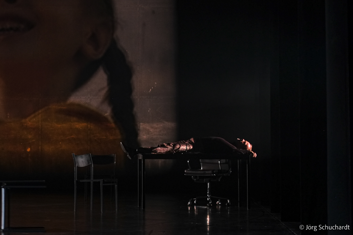 King Philip II of Spain laying on his desk, remembering the past in a dark scene, lighting design by Jörg Schuchardt, in a theatrical performance of Friedrich Schillers Drama Don Carlos at Staatstheater Stuttgart