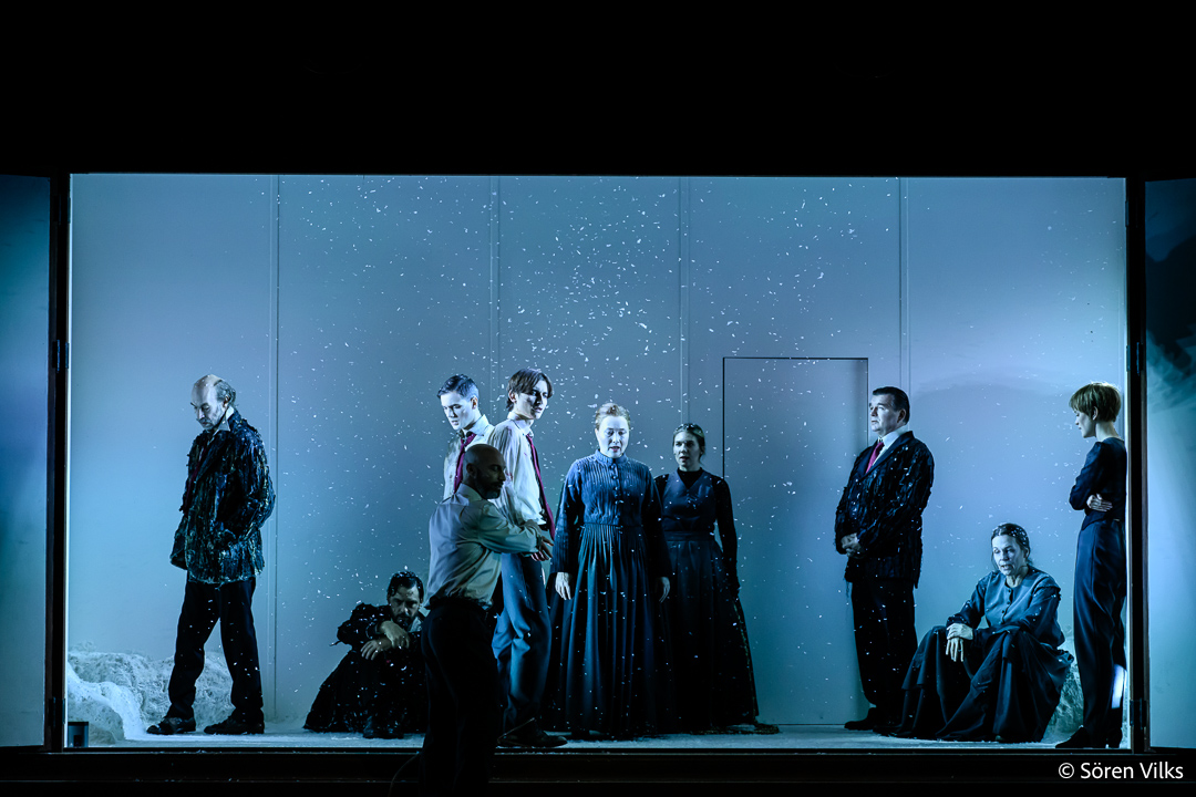 At Dramaten Stockholm, witness the gripping final act of 'Brott och Straff' as the cast finds themselves confined within an imposing cabinet. The harsh, wintry light exposes the interior as snow falls gently within. With a haunting chorus, the cabinet doors draw to a close, signaling a powerful conclusion to the scene.