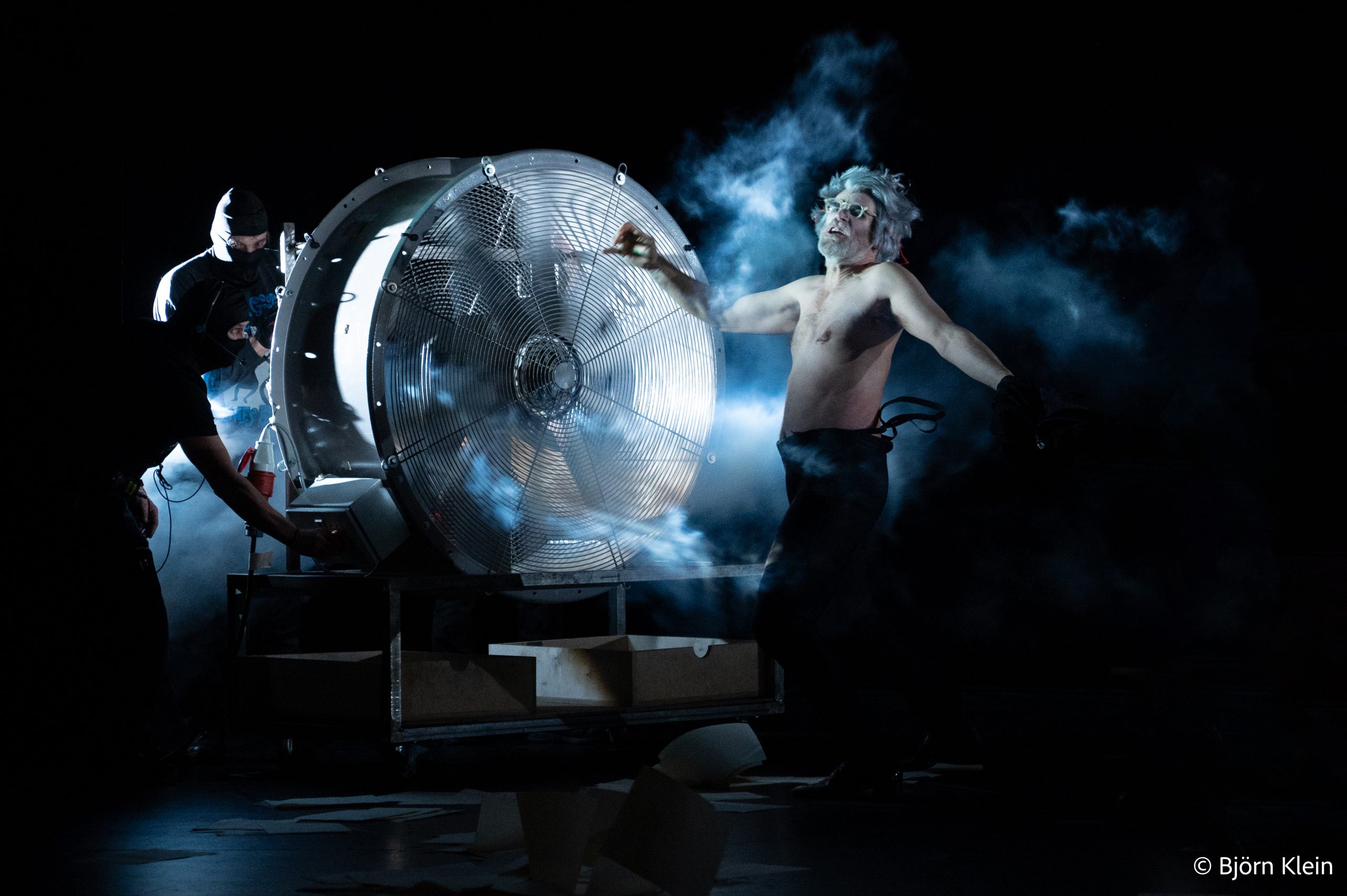 Intendant Geldoff vor einer großen Windmaschine im Theatersturm, perfekte Symbiose von Musik, Regie und Lichtdesign